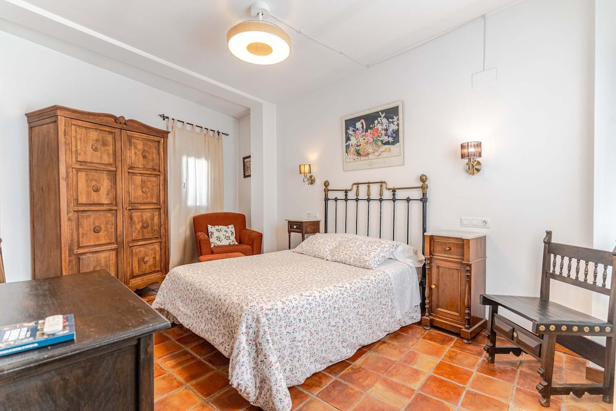 Un dormitorio con cama, armario de madera, una silla, mesita de noche y escritorio.