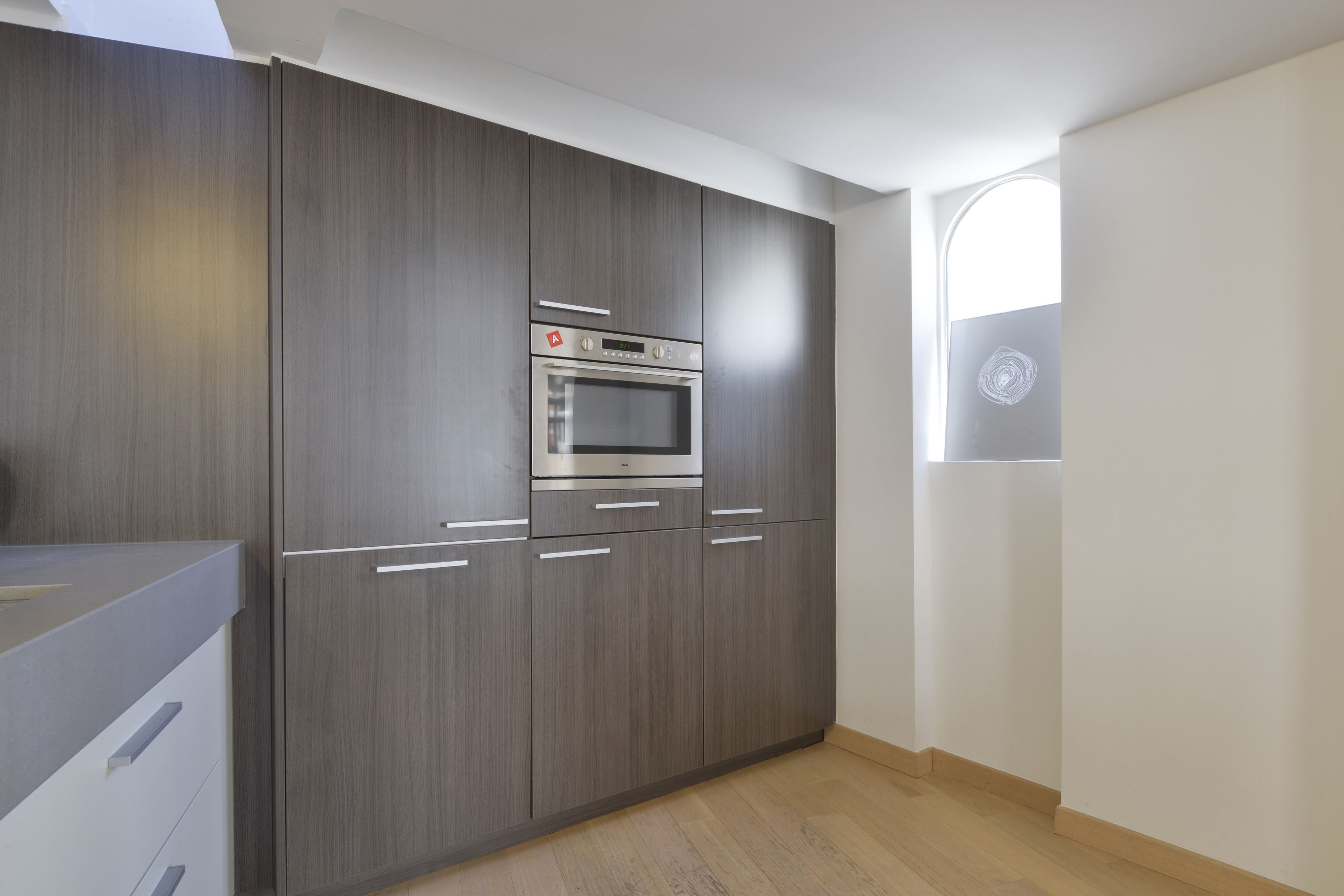 A modern kitchen with dark wood cabinets, a stainless steel oven, and a window with a circular design.
