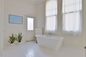 A spacious bathroom with a freestanding bathtub, two potted plants, a framed artwork on the wall, and large windows with sheer curtains. - Zurenborg Area Apartments (Antwerp)