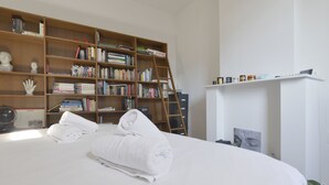 A neatly made bed with white linens, a wooden bookshelf filled with books, a ladder, and a small shelf with decorative items. - Zurenborg Area Apartments (Antwerp)
