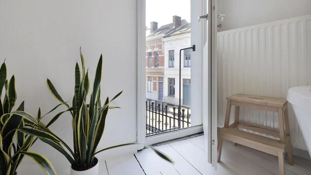 A balcony with a view of buildings, a wooden stool, and a potted plant. - Zurenborg Area Apartments (Antwerp)