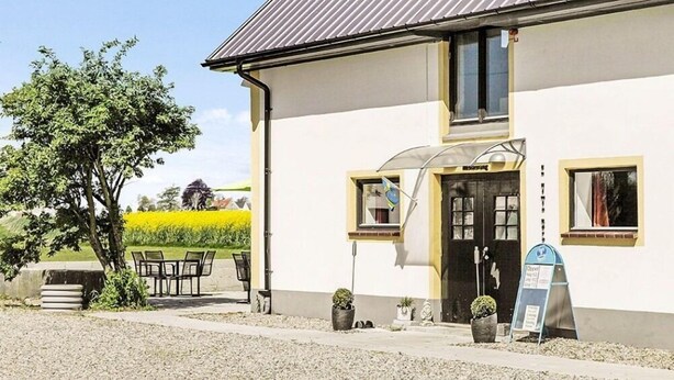 A building with a white exterior, a dark door, and a small window. There is a table and chairs outside, and a signboard is visible. - Hotel Borrby (Borrby)
