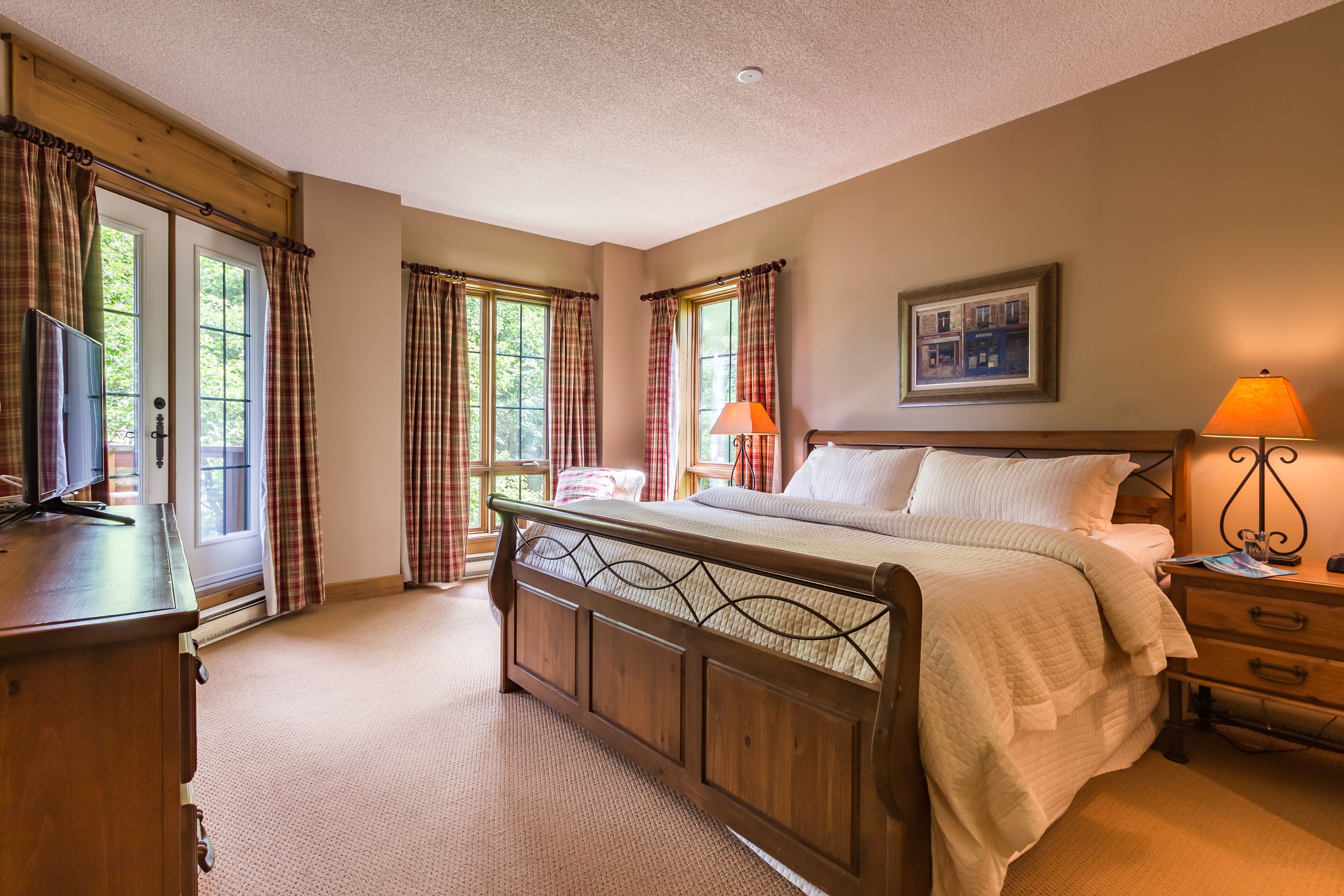 Une chambre à coucher avec un lit en bois, une table de chevet avec une lampe, une commode et une fenêtre avec des rideaux à carreaux.
