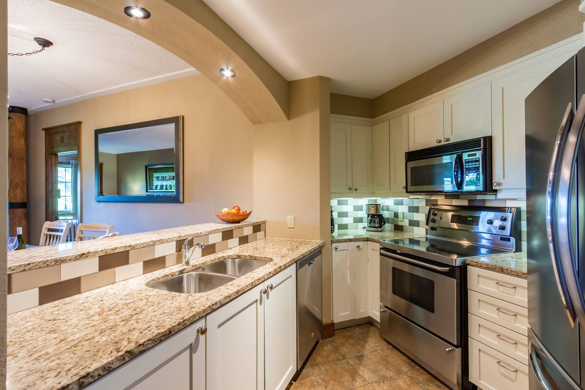 A kitchen with granite countertops, stainless steel appliances, and white cabinetry.