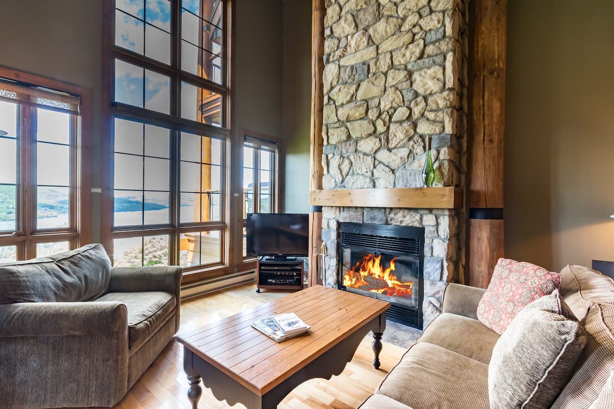 A cozy living room with a stone fireplace, large windows, and comfortable seating.