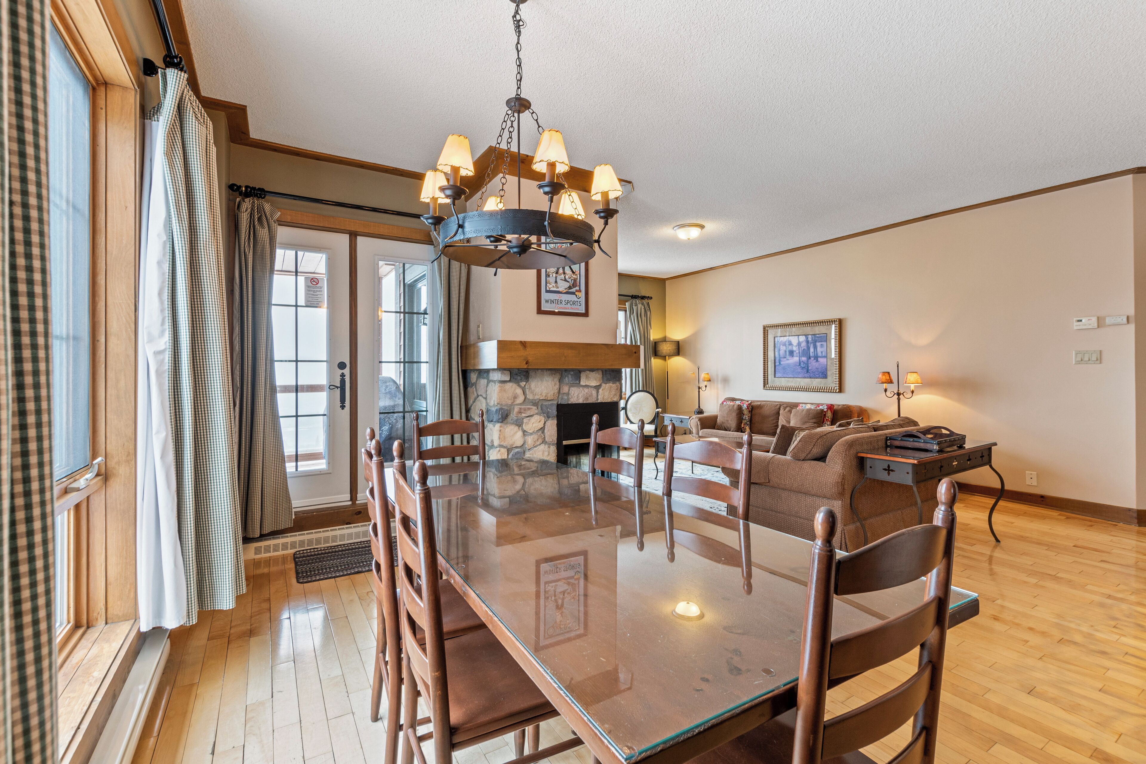 A spacious living room with a glass-top dining table, wooden chairs, a fireplace, and a cozy sofa.