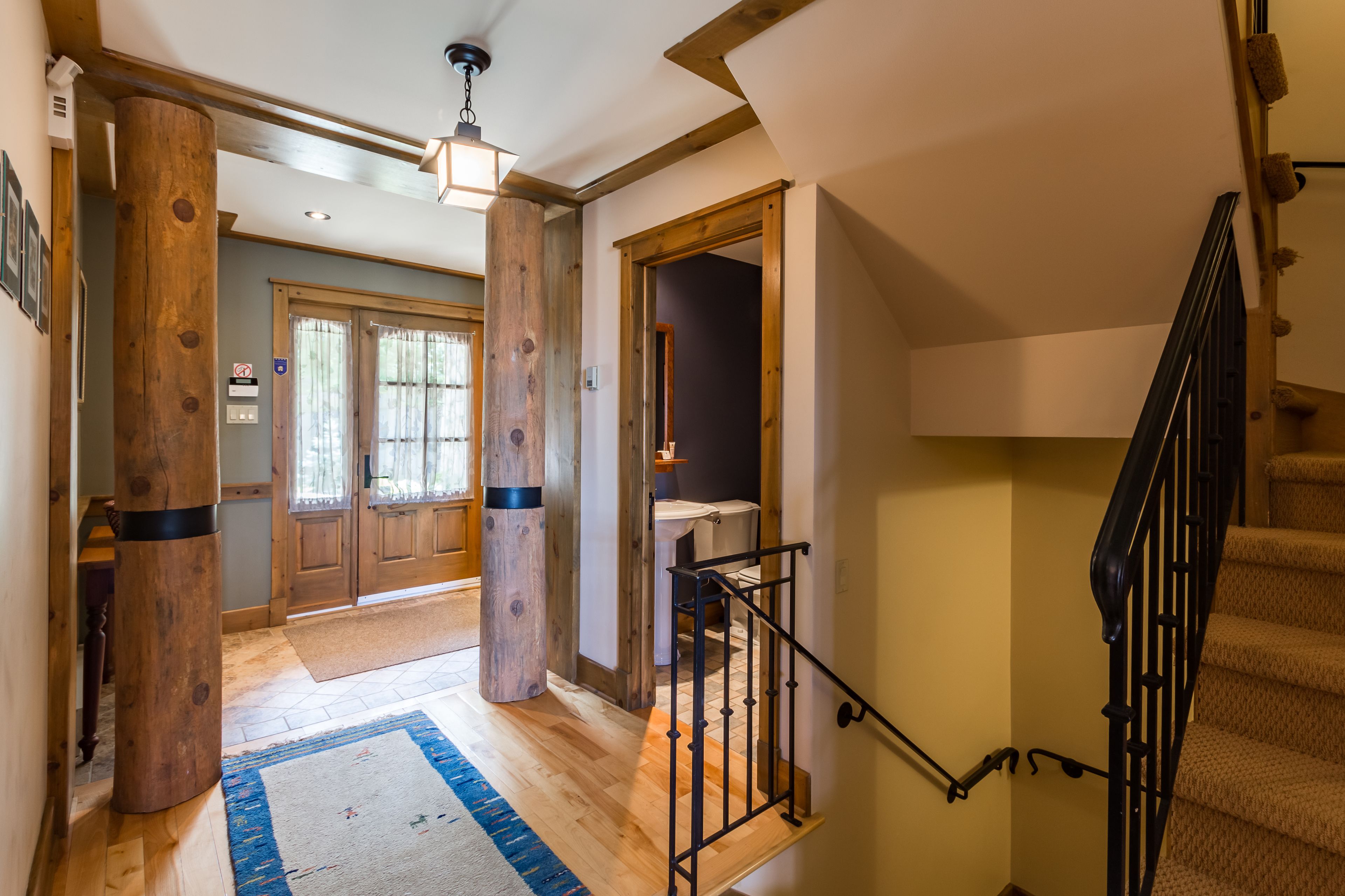 A wooden interior hallway with a staircase, a door with a window, and a light fixture.