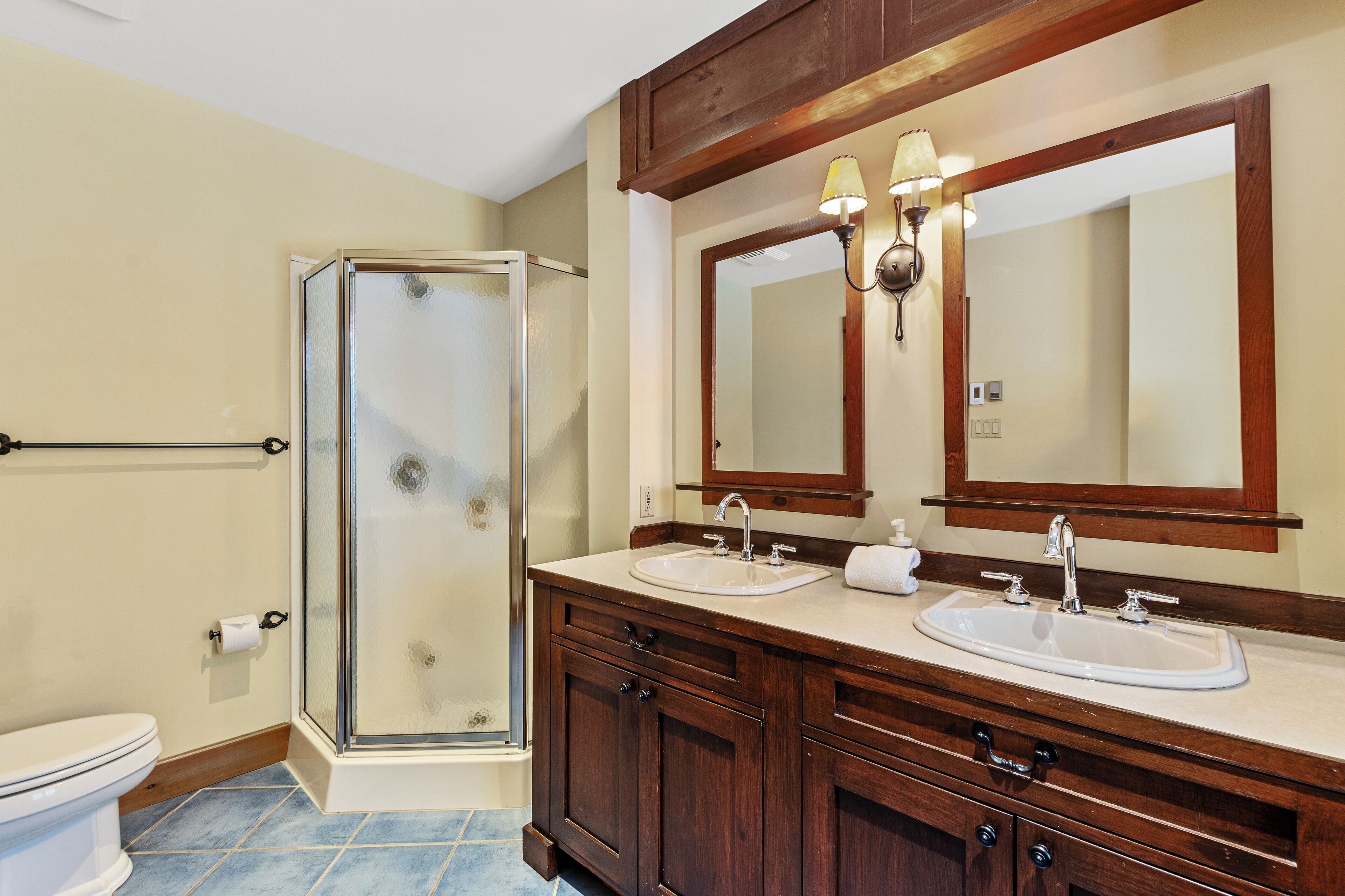 A bathroom with a glass shower enclosure, two sinks, a large mirror, and wooden cabinetry.