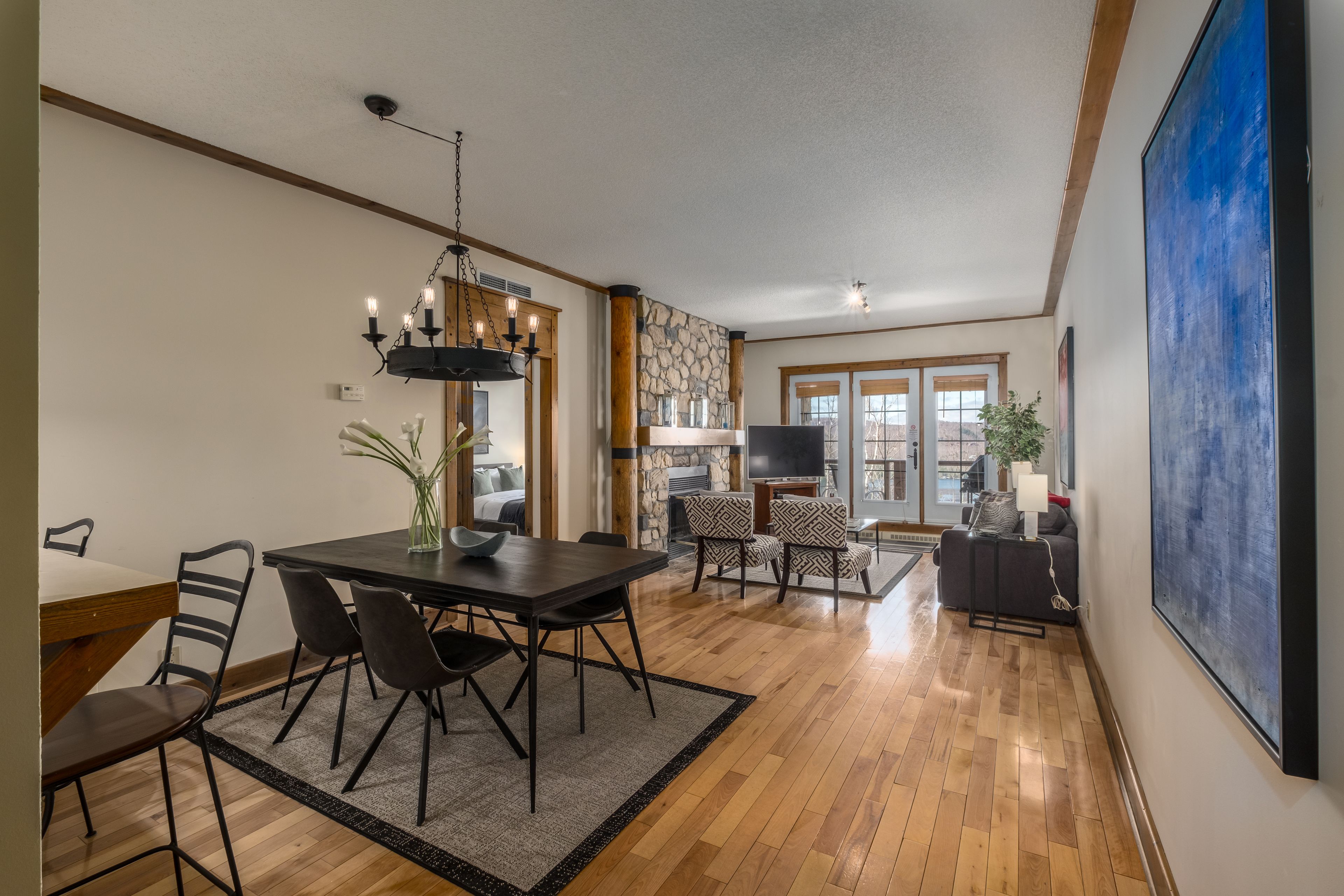 A spacious living area with a dining table, chairs, a fireplace, and a large painting on the wall.