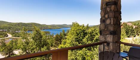 Ein Balkon mit Steinpfeiler, Holzwertlauf und Blick auf einen von Bäumen umgebenen See.