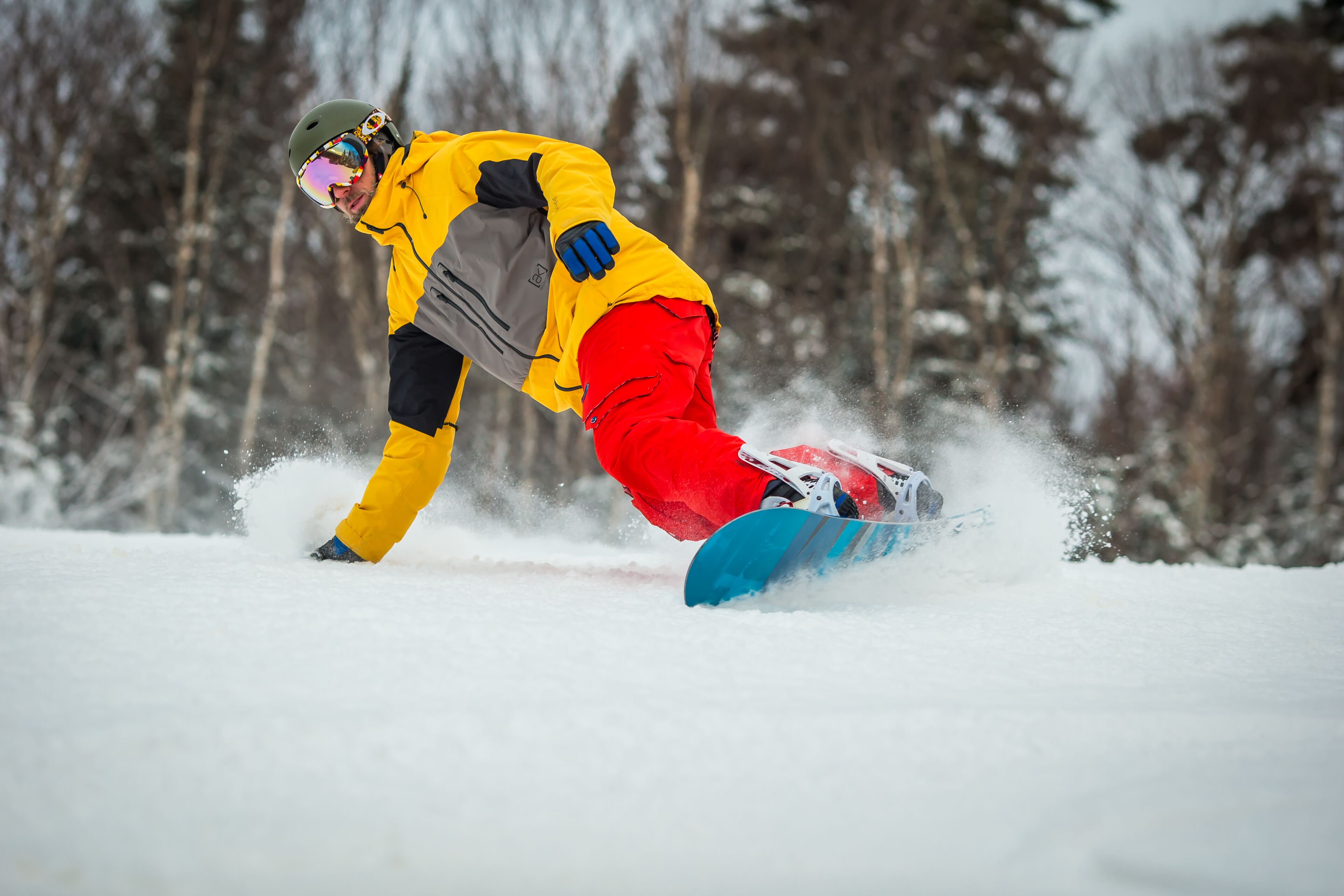 A snowboarder in a yellow and red outfit performing a turn on a snowy slope.
