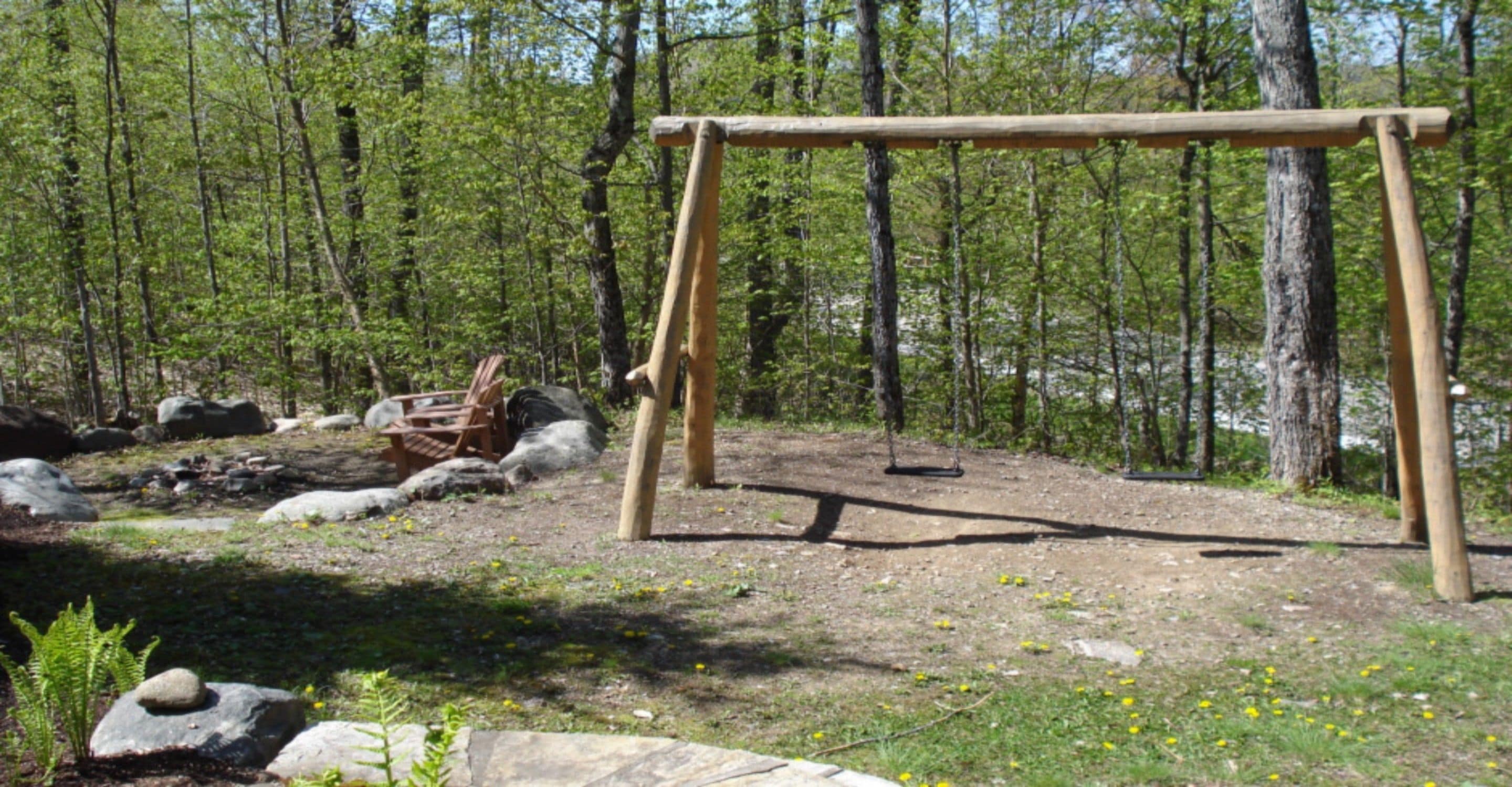 Une balançoire en bois installée dans une zone boisée, parsemée de rochers et de fougères.