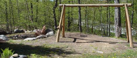 Une balançoire en bois installée dans une zone boisée, parsemée de rochers et de fougères.