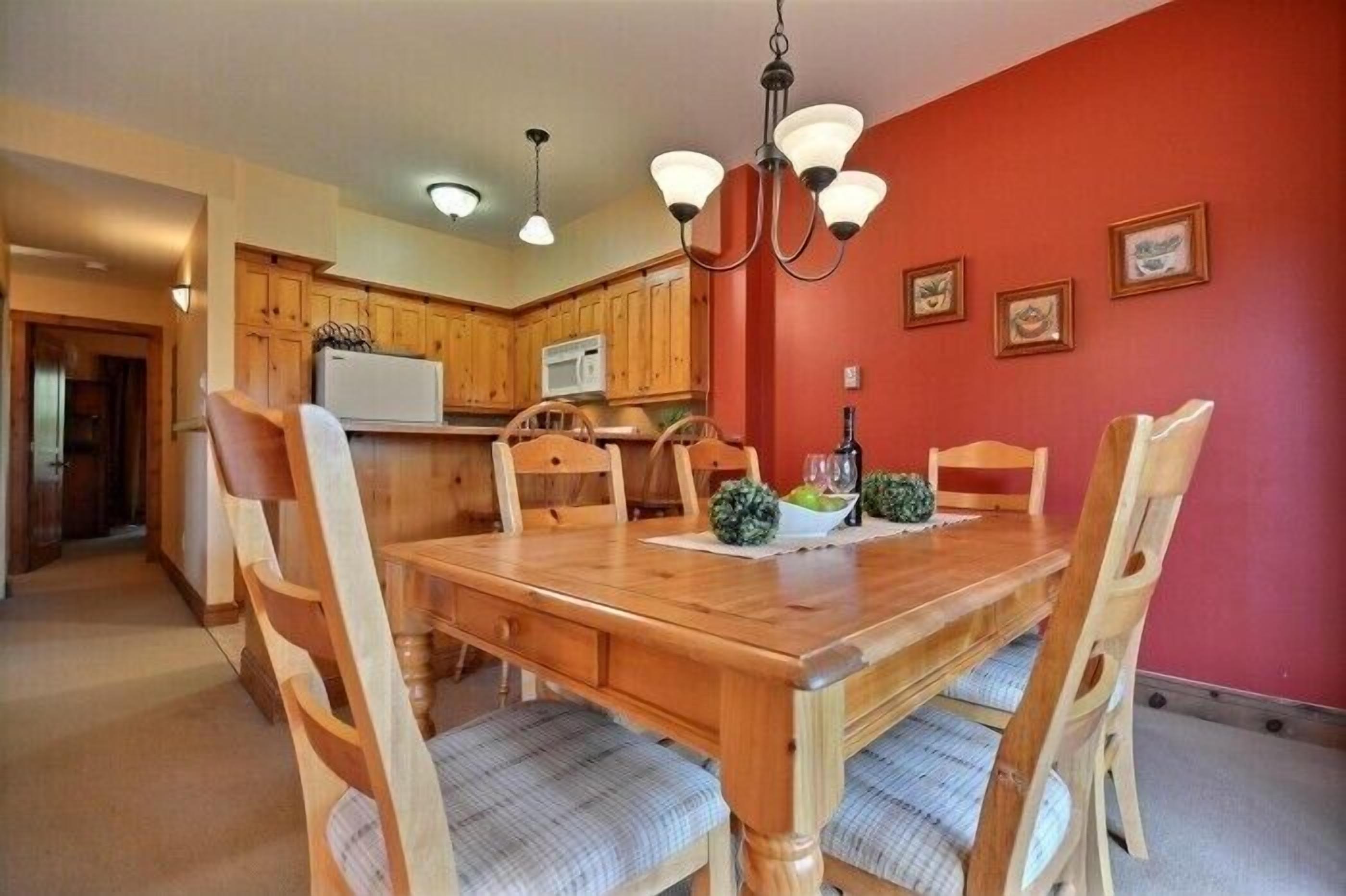 A dining area with a wooden table and chairs, a chandelier, and a red accent wall.