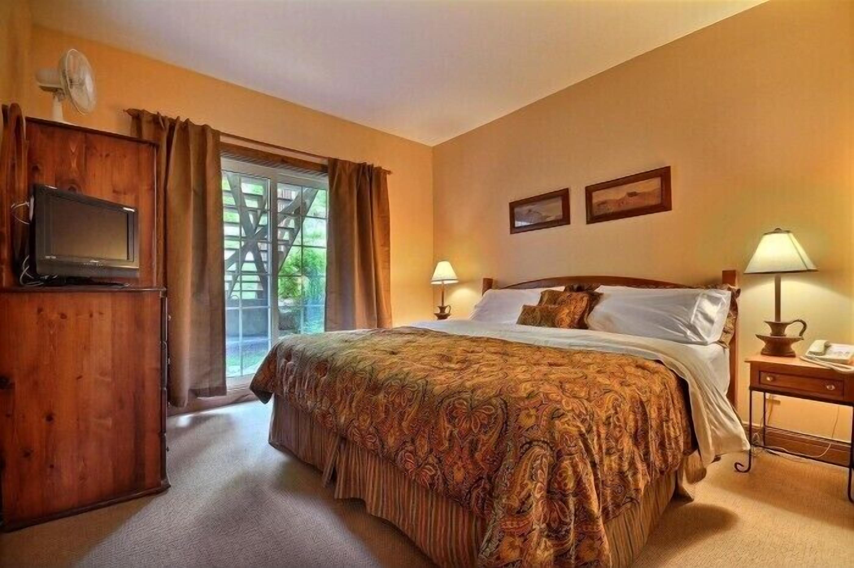 A bedroom with a bed, two bedside lamps, a TV, and a wooden cabinet.