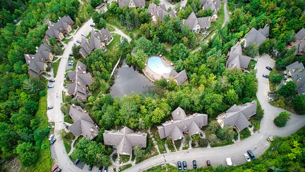 An aerial view of a residential area with houses, a swimming pool, and a road. - Le Plateau - RVMT (Mont-Tremblant)