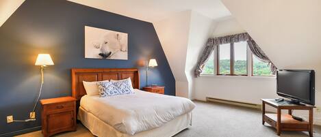 A bedroom with a bed, two bedside lamps, a TV on a stand, a painting on the wall, and a window with curtains.