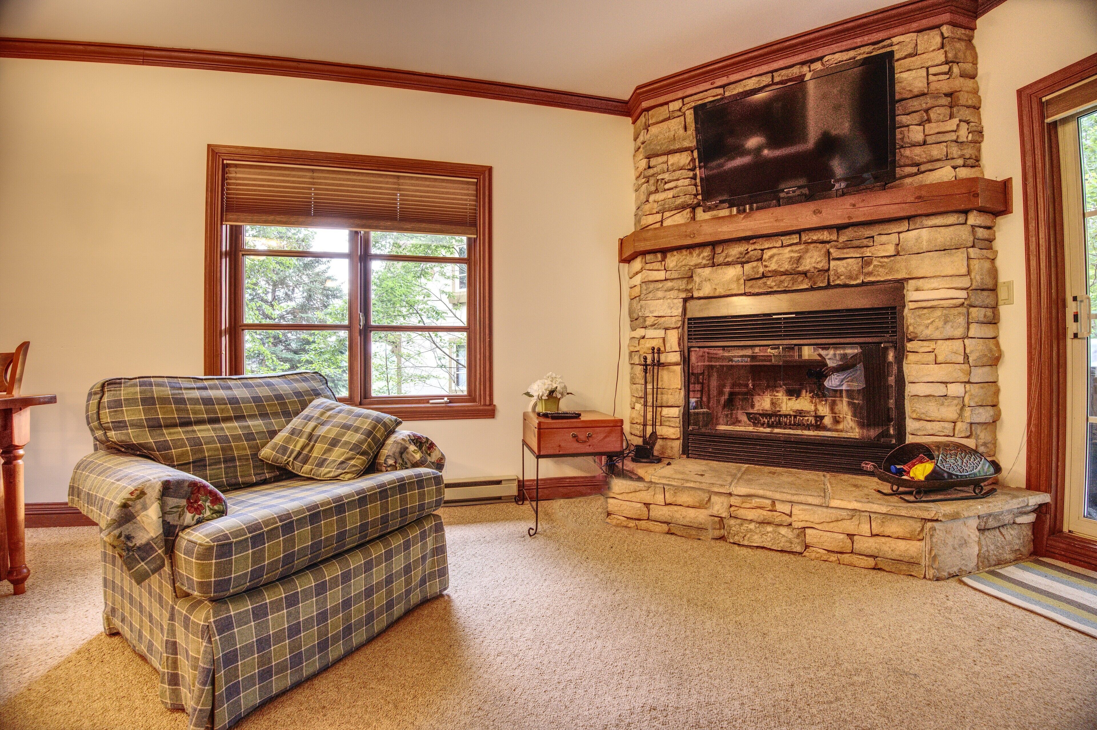 A living room with a plaid sofa, a stone fireplace, and a television mounted above it.