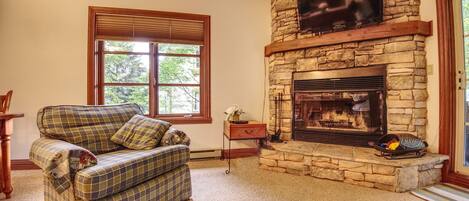 A living room with a plaid sofa, a stone fireplace, and a television mounted above it.