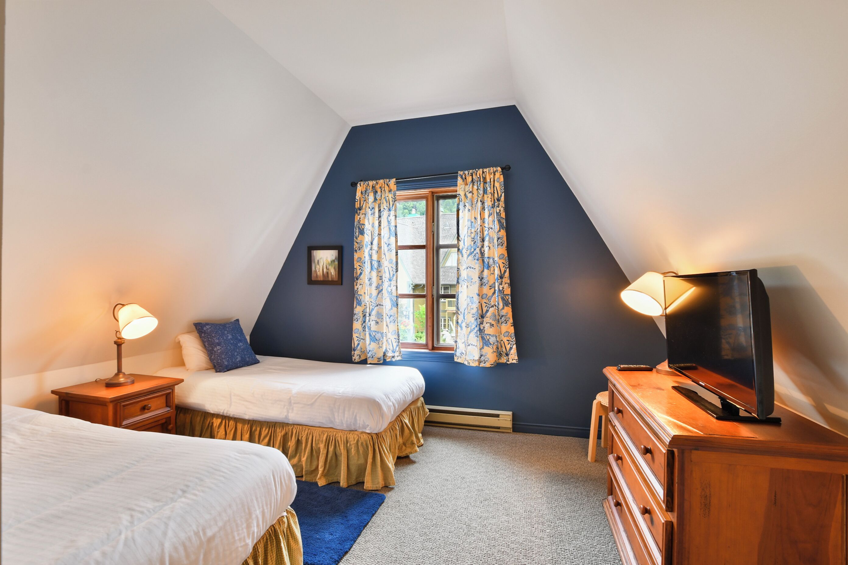 Una camera da letto con due letti, una televisione e una finestra con tende.