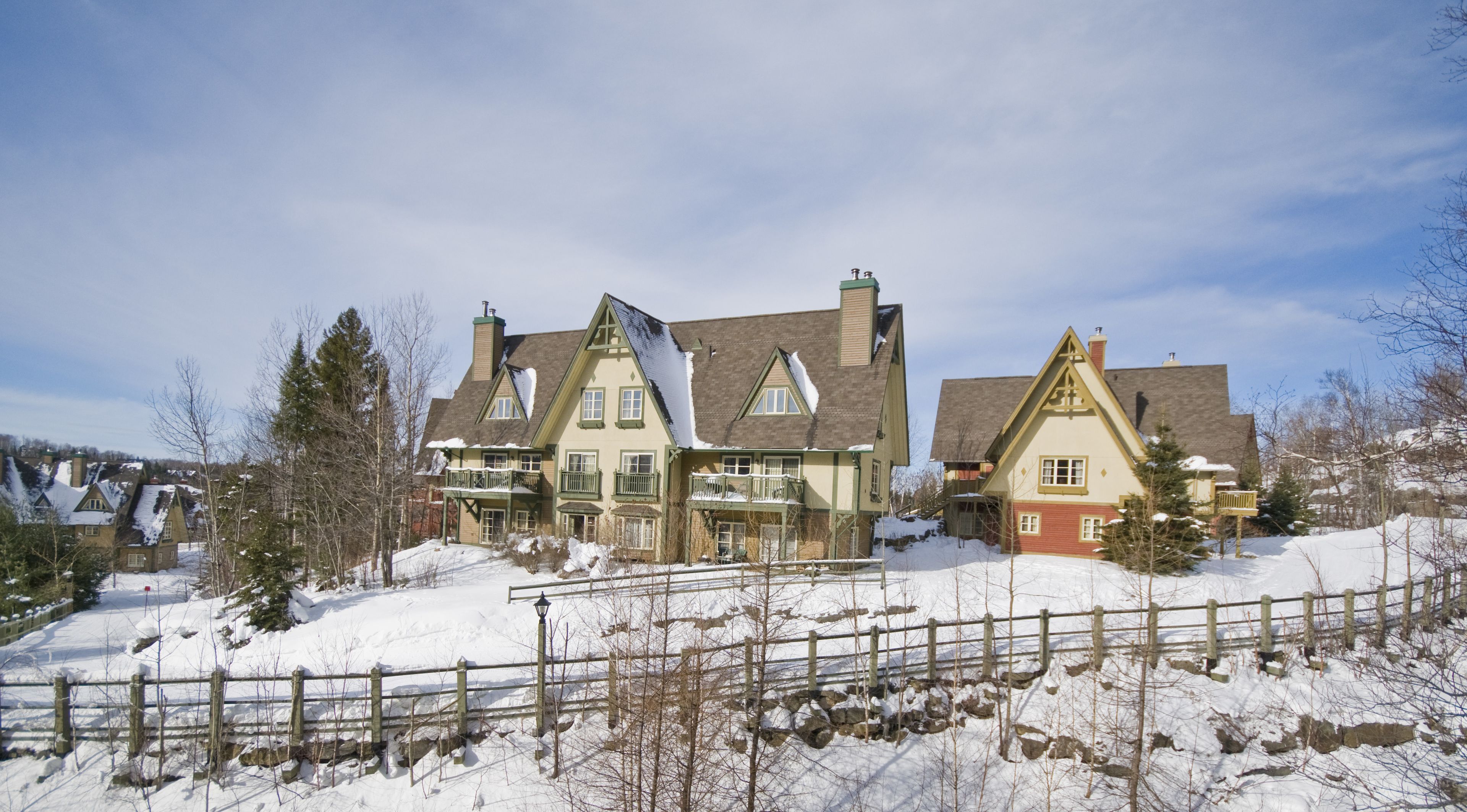 A large, multi-story house with a snow-covered roof and a stone wall in the foreground.