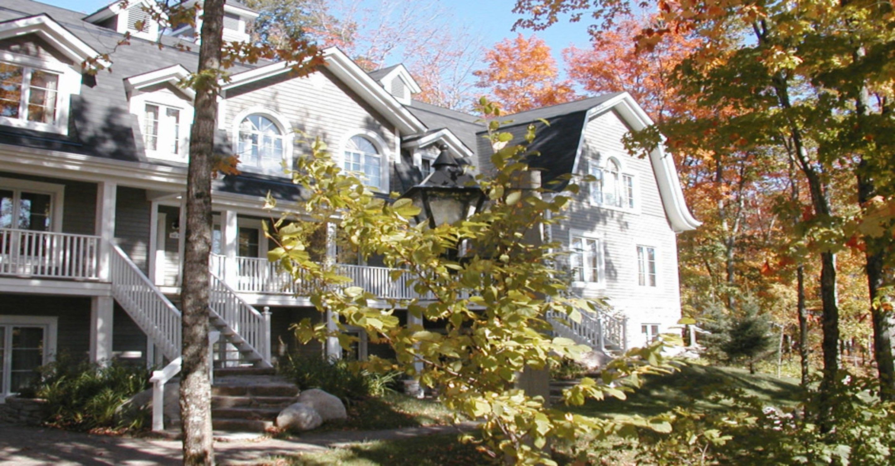 Une grande maison à deux étages, dotée d’un porche à l’avant, d’un escalier et d’une pelouse bien entretenue.