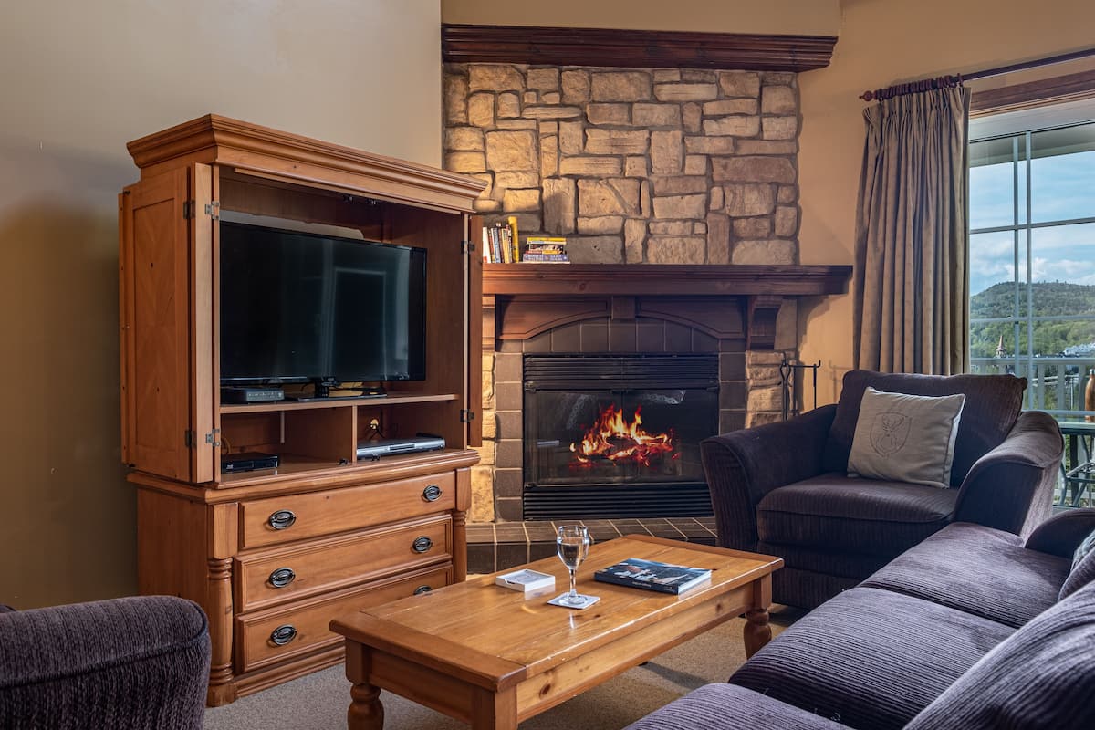 A cozy living room with a stone fireplace, a wooden entertainment unit, and comfortable seating.