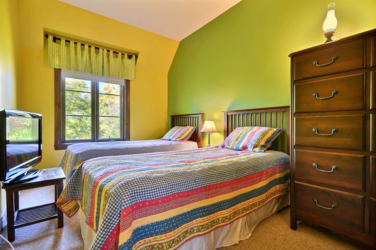 A bedroom with two beds, a dresser, a television, and a window with curtains.