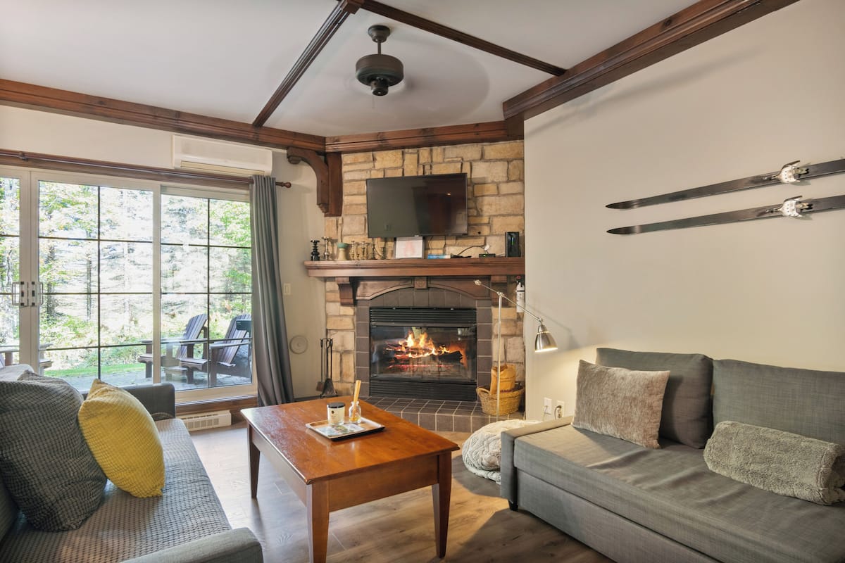 A cozy living room with a fireplace, a sofa, a coffee table, and a television mounted on a stone wall.