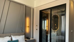 Habitación de hotel moderna con una cama grande, una mesita de noche con teléfono y cabina de ducha con paredes de vidrio.