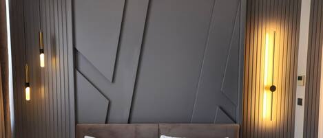 Une chambre d’hôtel moderne avec un grand lit, deux tables de chevet, une tête de lit ornée de motifs géométriques et des lampes fixées au mur.