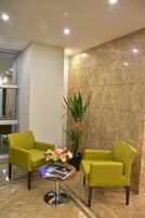 A reception area with two green chairs, a small table with a flower arrangement, and a potted plant.