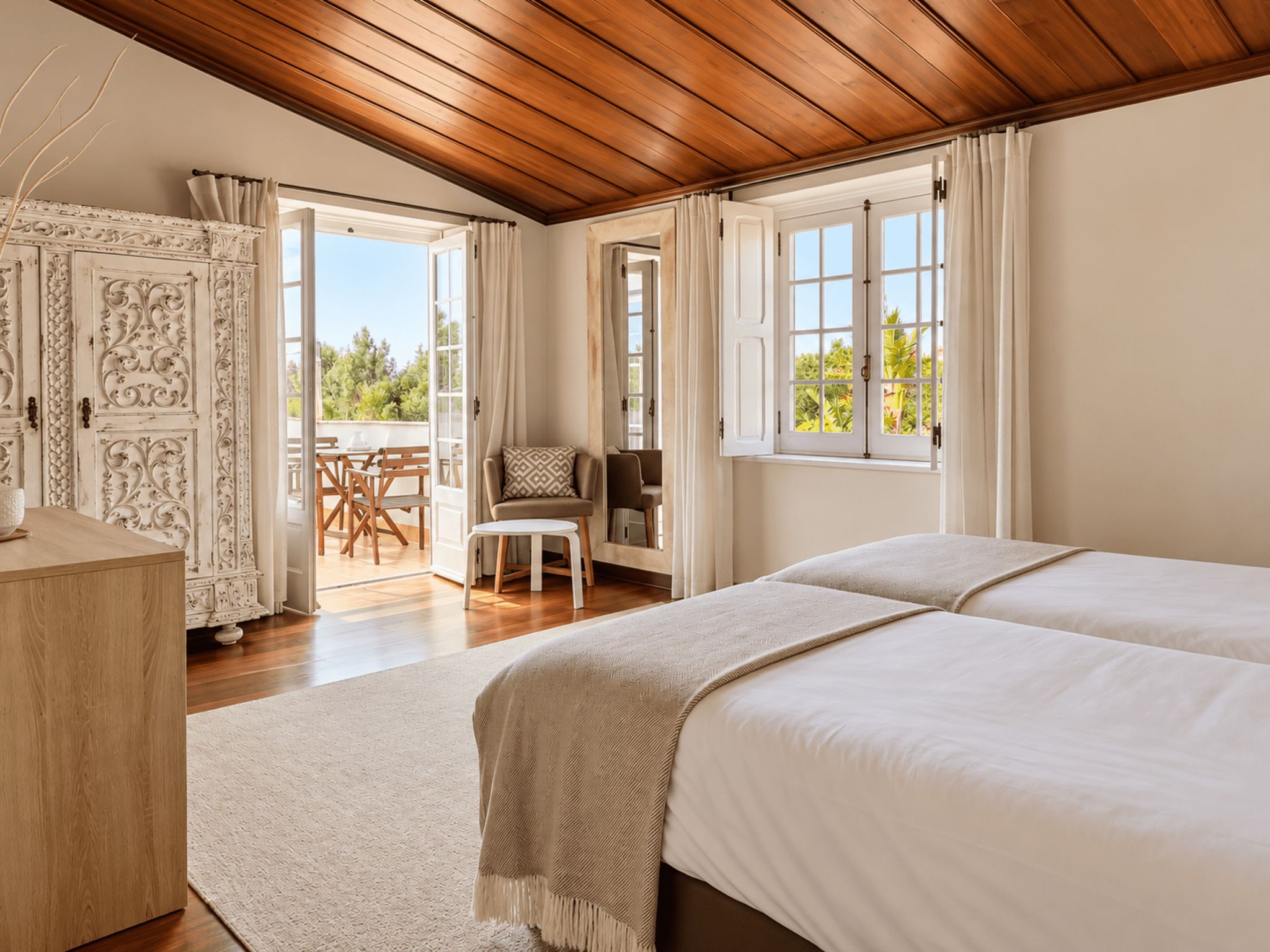 Un dormitorio con dos camas, techo de madera, balcón con mesa y sillas, y vistas a zonas verdes.