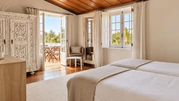 Un dormitorio con dos camas, techo de madera, balcón con mesa y sillas, y vistas a zonas verdes.