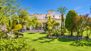 A white building with a tiled roof, surrounded by a well-maintained garden with various plants and a lawn. - Vila Louro (Torres Vedras)