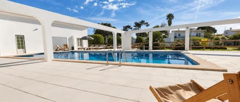 A pool area with a clear blue sky, white walls, and a wooden deck.