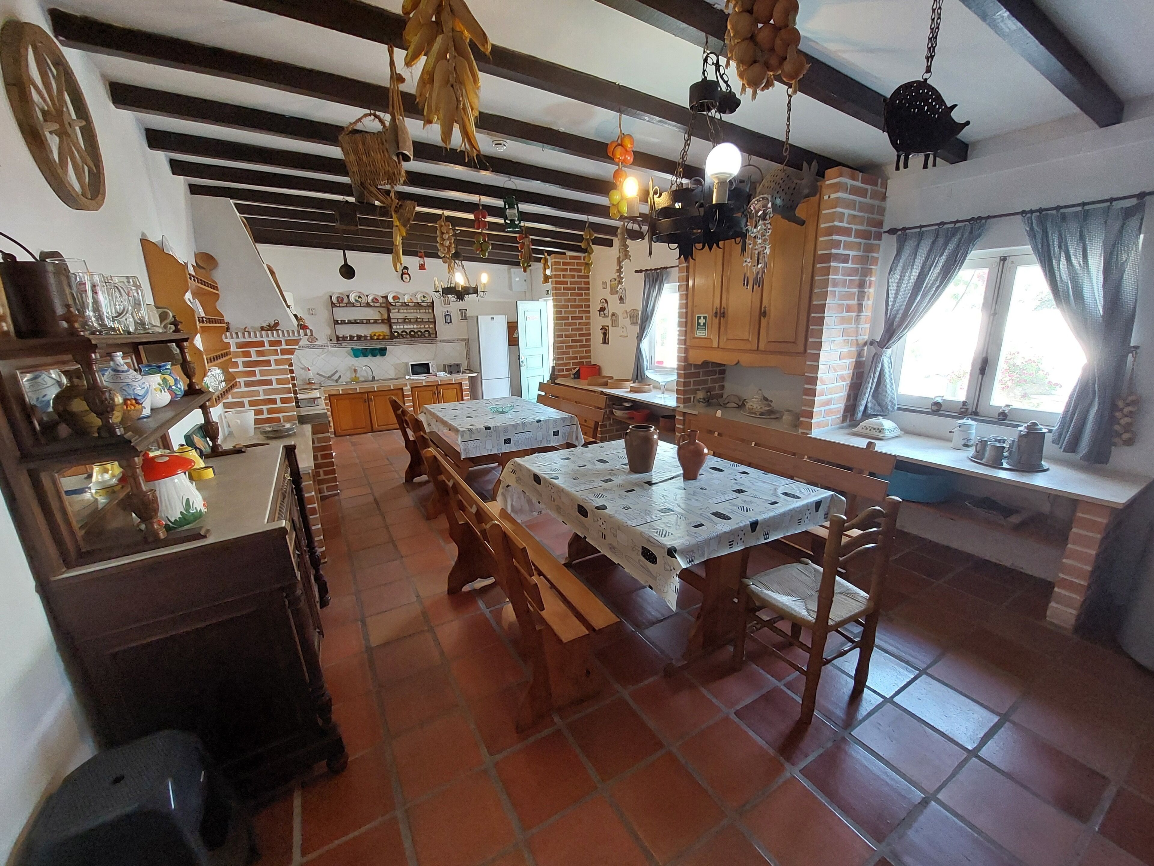 A rustic kitchen with exposed brick walls, wooden beams, and a large dining table with benches.