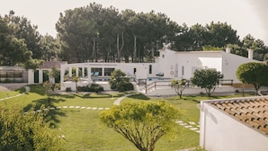 Un edificio moderno de color blanco con piscina, rodeado de césped cuidado y árboles.