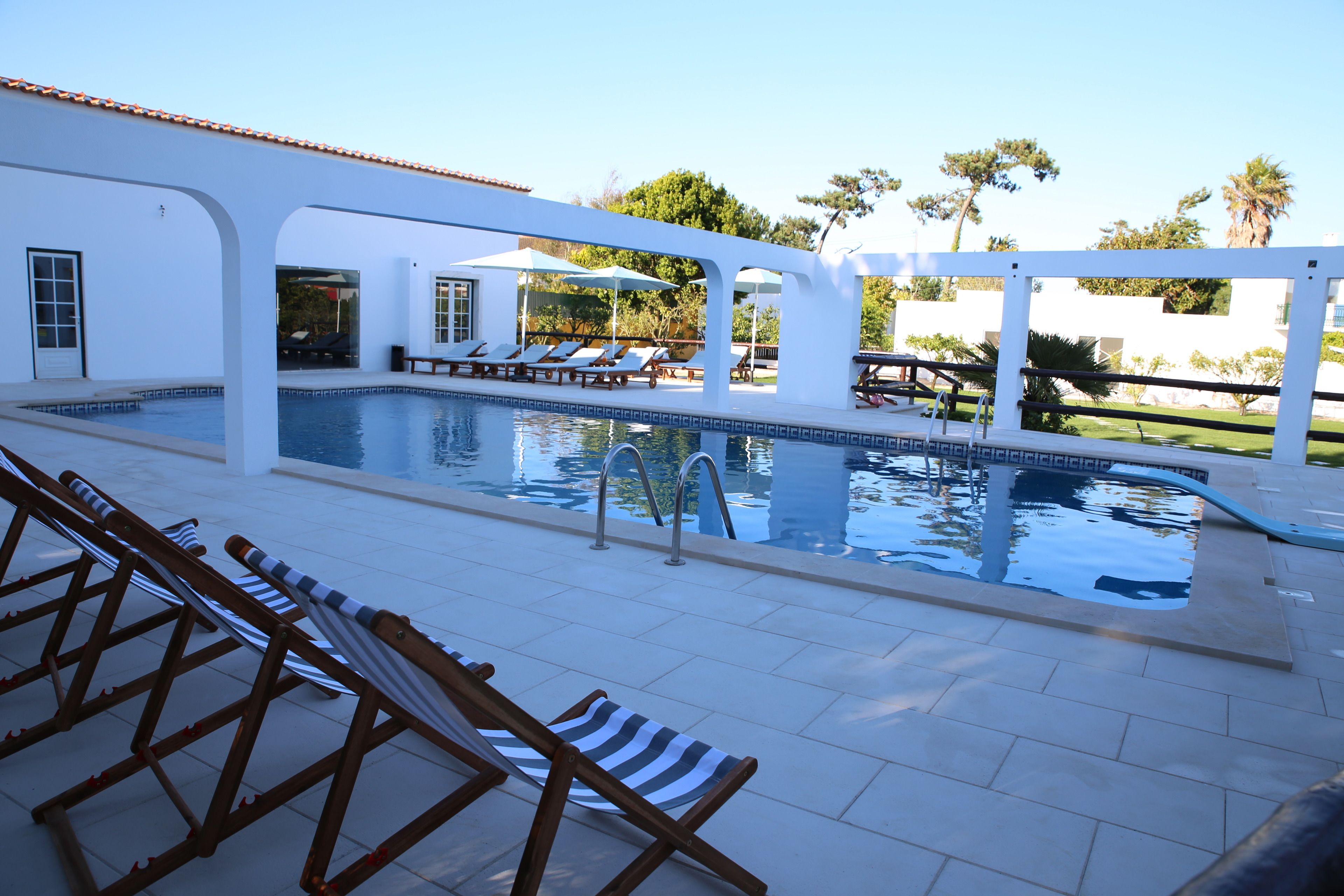 A pool area with lounge chairs, a pool, and a covered seating area.