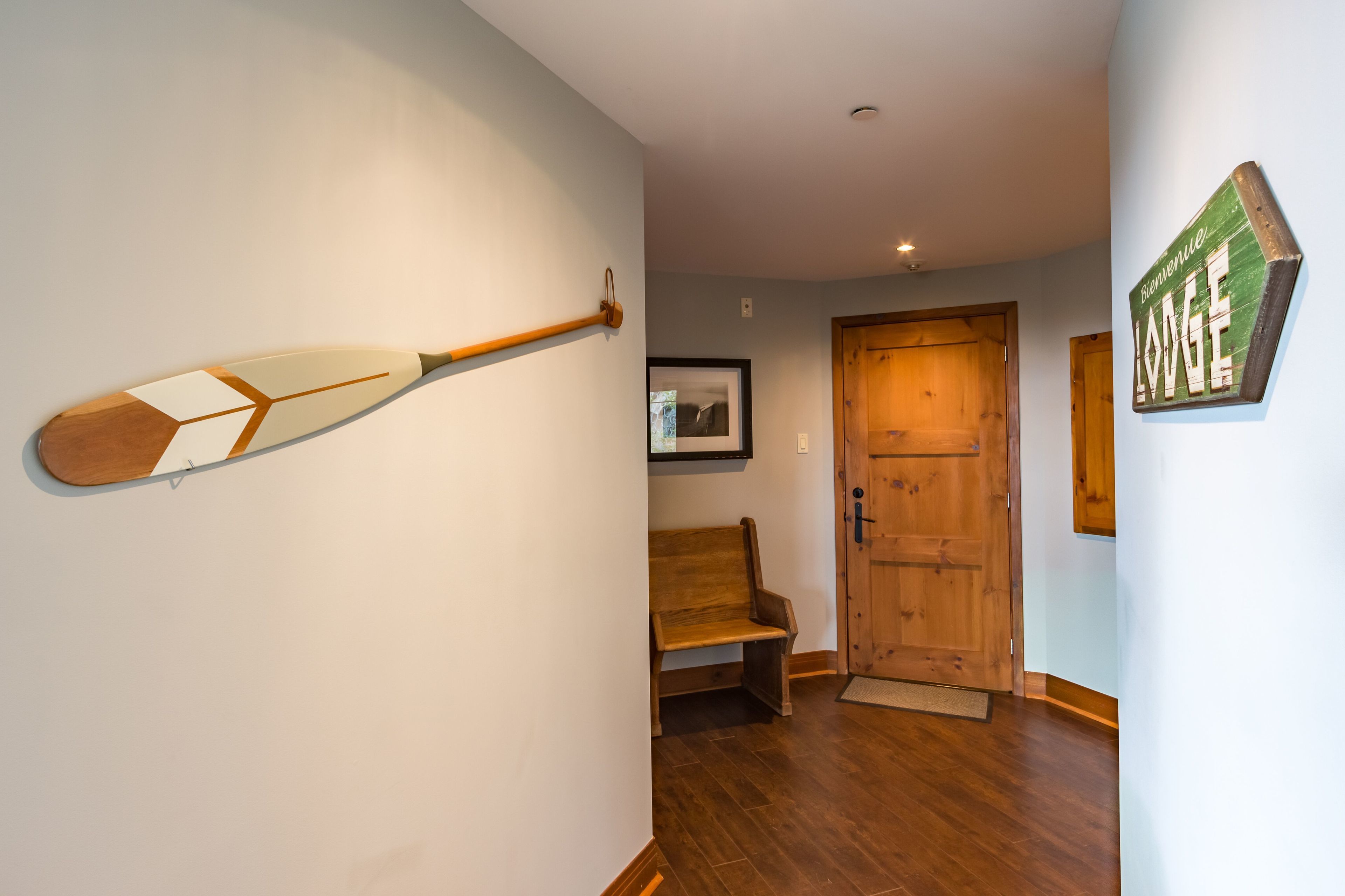 A hallway with wooden flooring, a wooden bench, a door, and a wall-mounted sign.