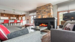 Una sala de estar moderna con chimenea de piedra, sofás grises y un televisor de pantalla plana.