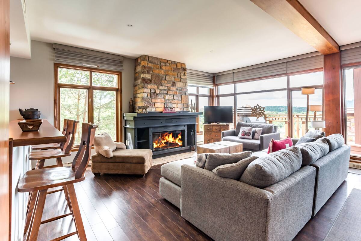 A spacious living room with a stone fireplace, a dining area with wooden chairs, and a large gray sofa.