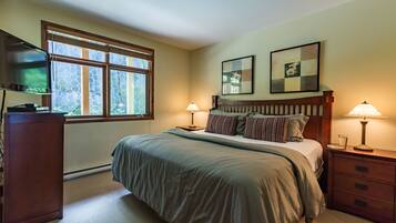 A bedroom with a large bed, two bedside lamps, a TV, and a window with a view of trees.