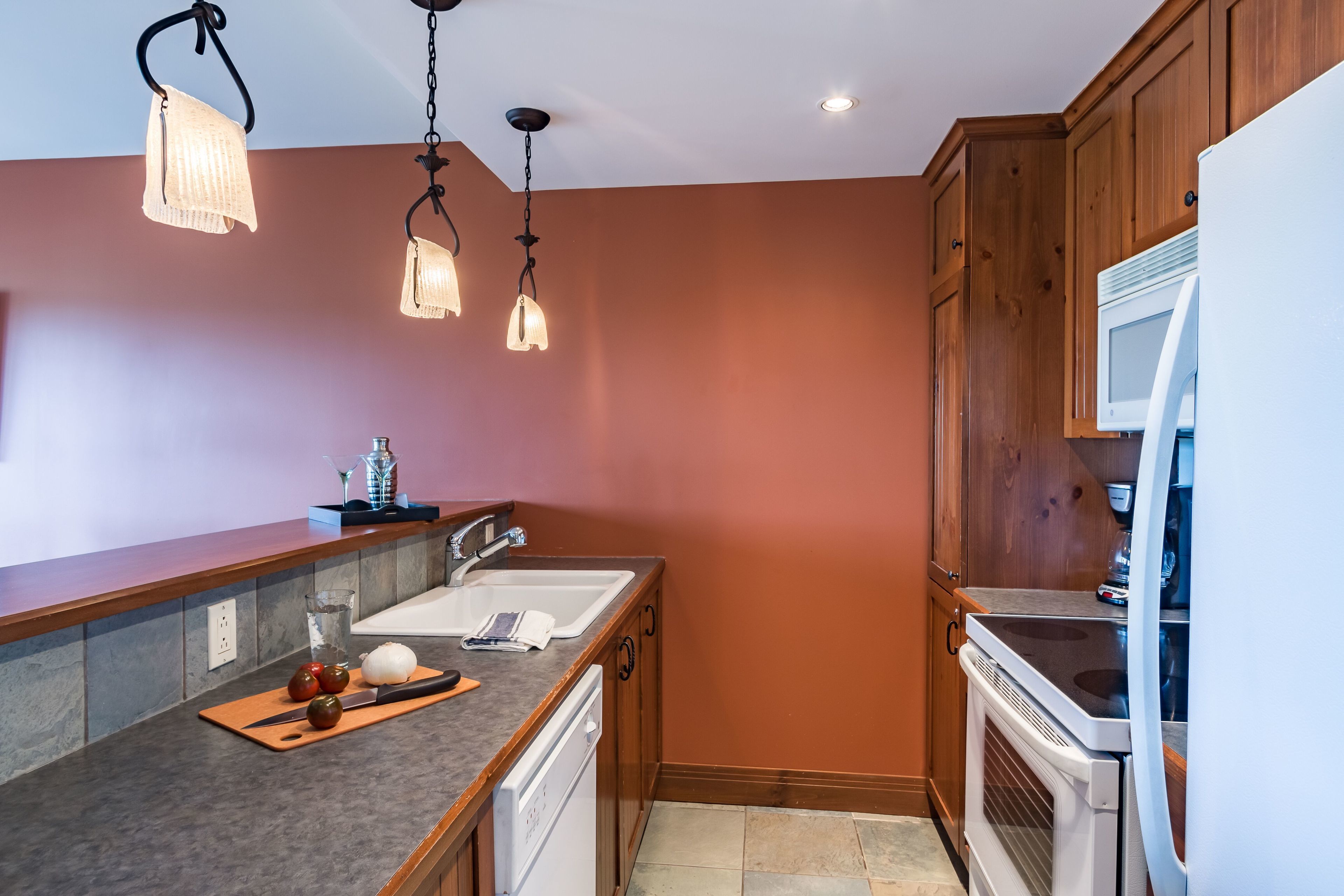 A kitchen with wooden cabinets, a double sink, a microwave, and a stove.