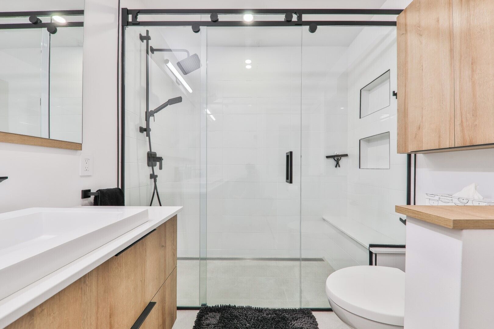 Un baño moderno con ducha de vidrio, lavamanos blanco y retrete.