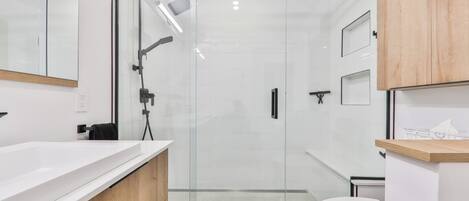 Un baño moderno con ducha de vidrio, lavamanos blanco y retrete.