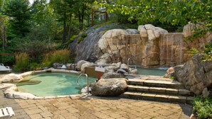 Un'area termale naturale con una piscina, scalinate che conducono a una cascata e vegetazione circostante.