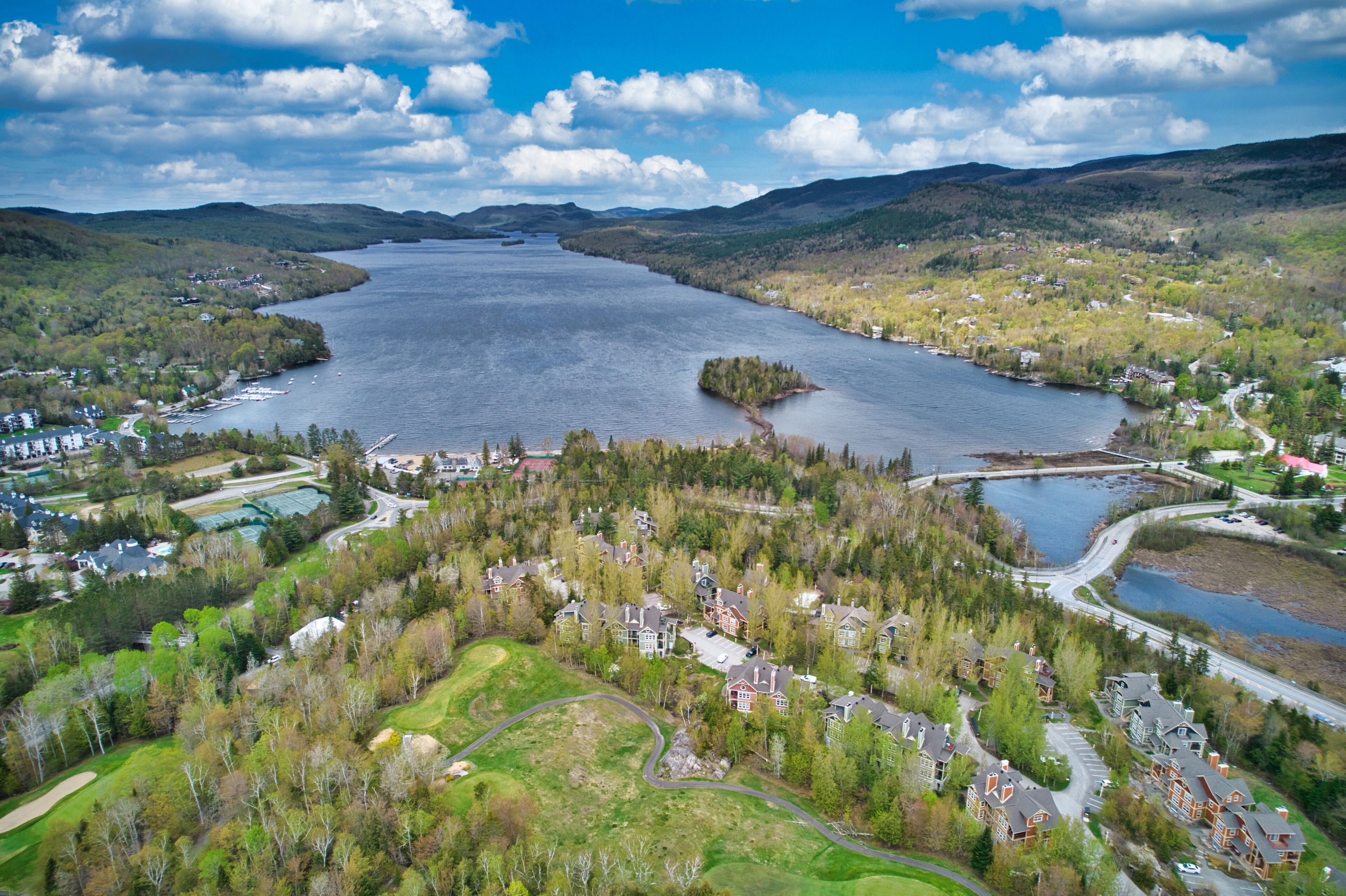 Vista aérea de una comunidad a orillas de un lago, con edificios residenciales, caminos y una pequeña isla en el lago.