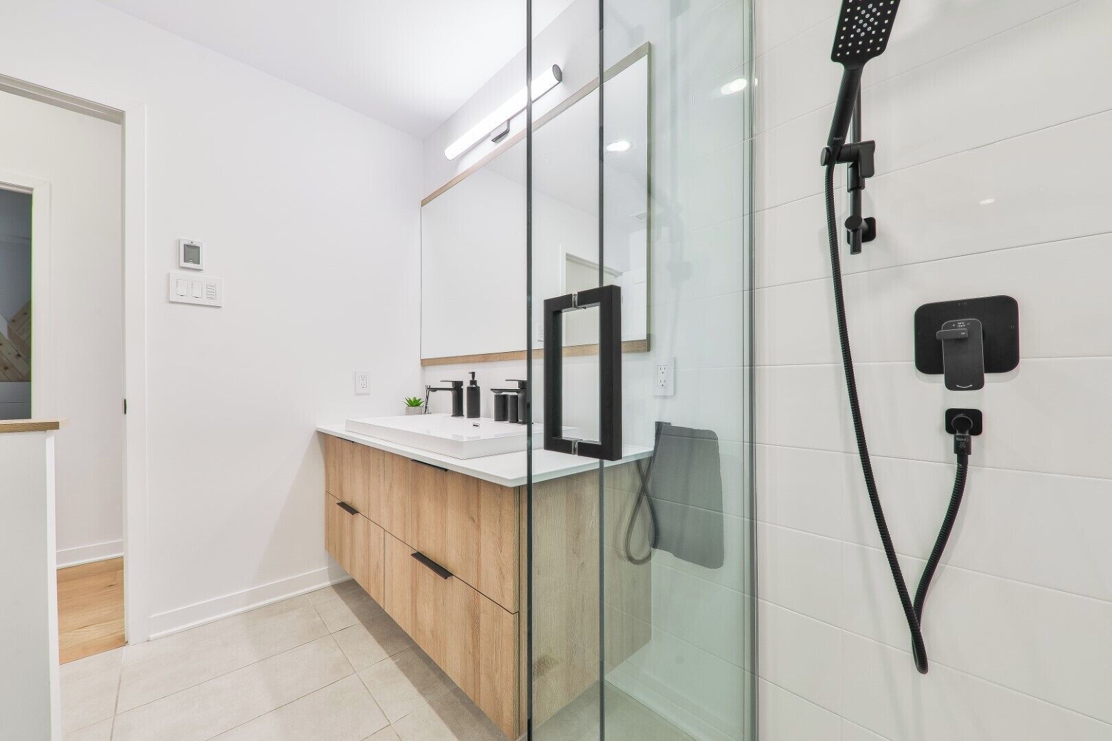 A modern bathroom with a glass shower enclosure, a white vanity with a wooden cabinet, and a large mirror.