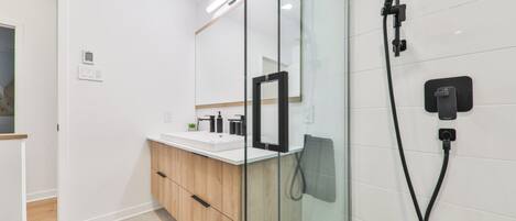A modern bathroom with a glass shower enclosure, a white vanity with a wooden cabinet, and a large mirror.